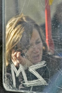 Telefonierende Frau hinter zerkratztem Straßenbahnfenster, © Petra Simon